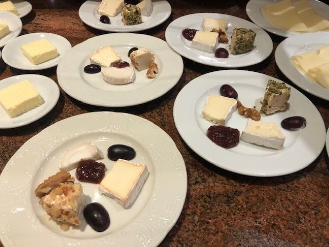 Several plates with different types of cheese, grapes, walnuts and jam arranged on a brown table., © Kronen Hotel GmbH