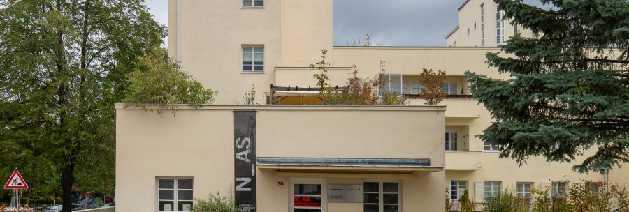 Beige Architekturgalerie mit Flachdach, Balkonen und Bäumen davor., © Thomas Fütterer Beige Architekturgalerie mit Flachdach, Balkonen und Bäumen davor., © Thomas Fütterer
