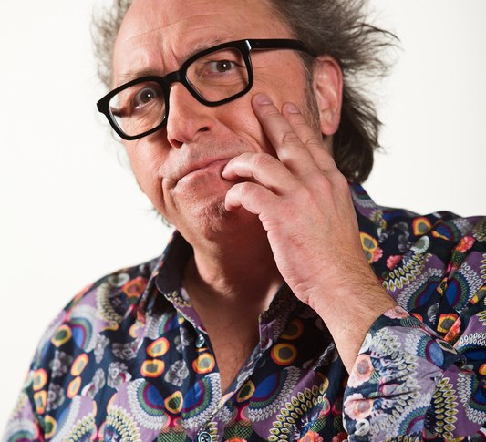 Ein Mann mit zerzaustem Haar und bunter Hemdbluse denkt nach. Er tr&auml;gt eine Brille und hat eine Hand am Kinn., &copy; Theaterhaus Stuttgart e.V.