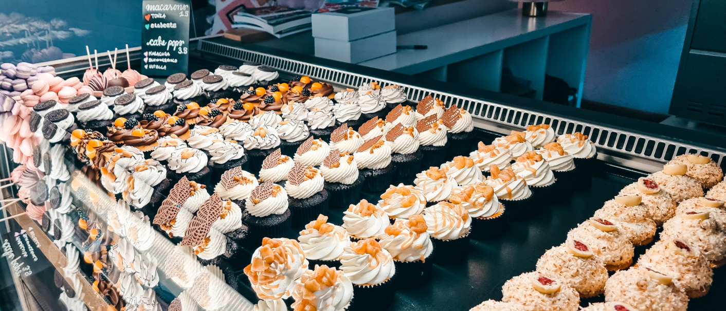 Eine Vitrine voller bunter Cupcakes und Macarons, kunstvoll dekoriert mit Sahne und Schokolade., © Cupcakes & Bagels, Stuttgart Eine Vitrine voller bunter Cupcakes und Macarons, kunstvoll dekoriert mit Sahne und Schokolade., © Cupcakes & Bagels, Stuttgart