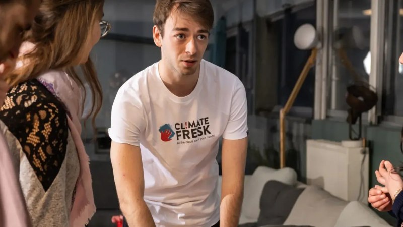Ein Mann im Climate Fresk T-Shirt erkl&auml;rt etwas in einem Workshop. Zwei Frauen h&ouml;ren aufmerksam zu. Der Raum ist modern eingerichtet., &copy; Climate Fresk Deutschland e. V.