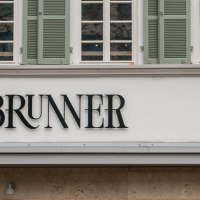Lettering on the facade of the Brunner restaurant with serifs. Above it, lattice windows with green shutters., &copy; SMG, Sarah Schmid