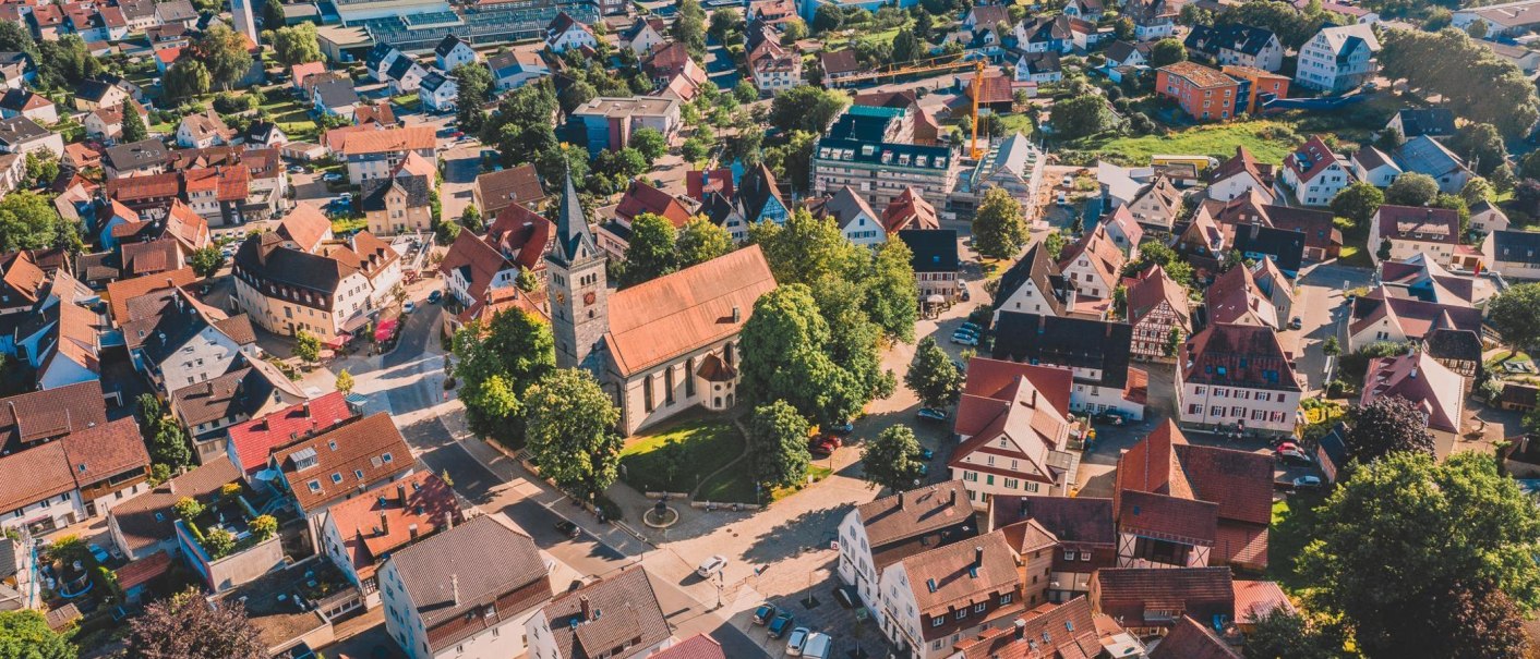 An aerial view of a small town with a church in the center, surrounded by houses and green trees., &copy; Sandra Bihlmaier - Stadt Welzheim