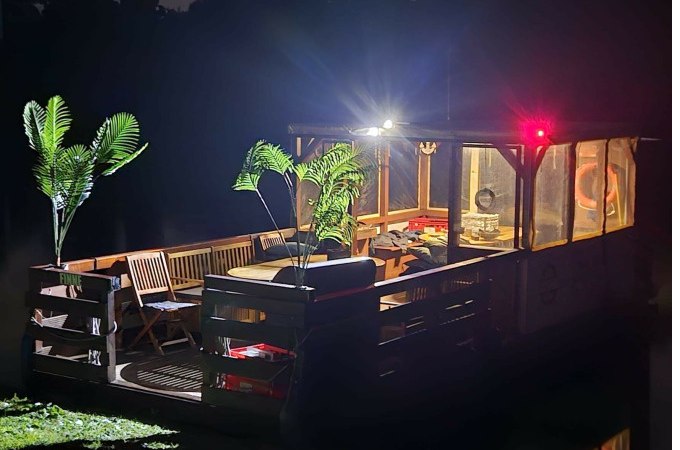 Ein beleuchtetes Floß mit Pflanzen und Möbeln auf einem dunklen Gewässer bei Nacht., © Cool-Tours StattReisen Ein beleuchtetes Floß mit Pflanzen und Möbeln auf einem dunklen Gewässer bei Nacht., © Cool-Tours StattReisen