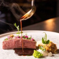An artfully prepared gourmet dish with meat, vegetables and a dark sauce that is poured onto the plate from a ladle., © 5 - Stuttgart