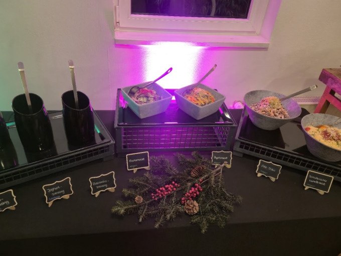 Ein Buffet mit verschiedenen Salaten in Schalen, dekoriert mit Tannenzweigen und Beeren. Kleine Tafeln beschreiben die Gerichte., &copy; Cool-Tours StattReisen