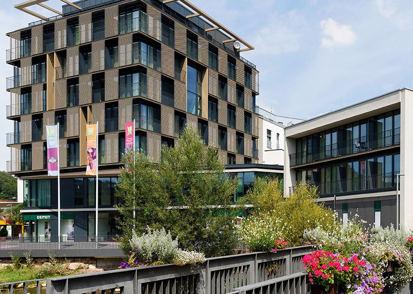 Modernes Hotelgebäude mit Glasfassade und Balkonen, umgeben von Pflanzen und Blumen auf einer Brücke., © TOMAS Modernes Hotelgebäude mit Glasfassade und Balkonen, umgeben von Pflanzen und Blumen auf einer Brücke., © TOMAS
