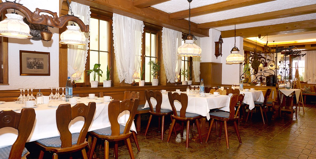 Gemütliches Restaurant mit Holzmöbeln, gedeckten Tischen und dekorativen Lampen. Weiße Vorhänge und Pflanzen schmücken die Fenster., © TOMAS Gemütliches Restaurant mit Holzmöbeln, gedeckten Tischen und dekorativen Lampen. Weiße Vorhänge und Pflanzen schmücken die Fenster., © TOMAS