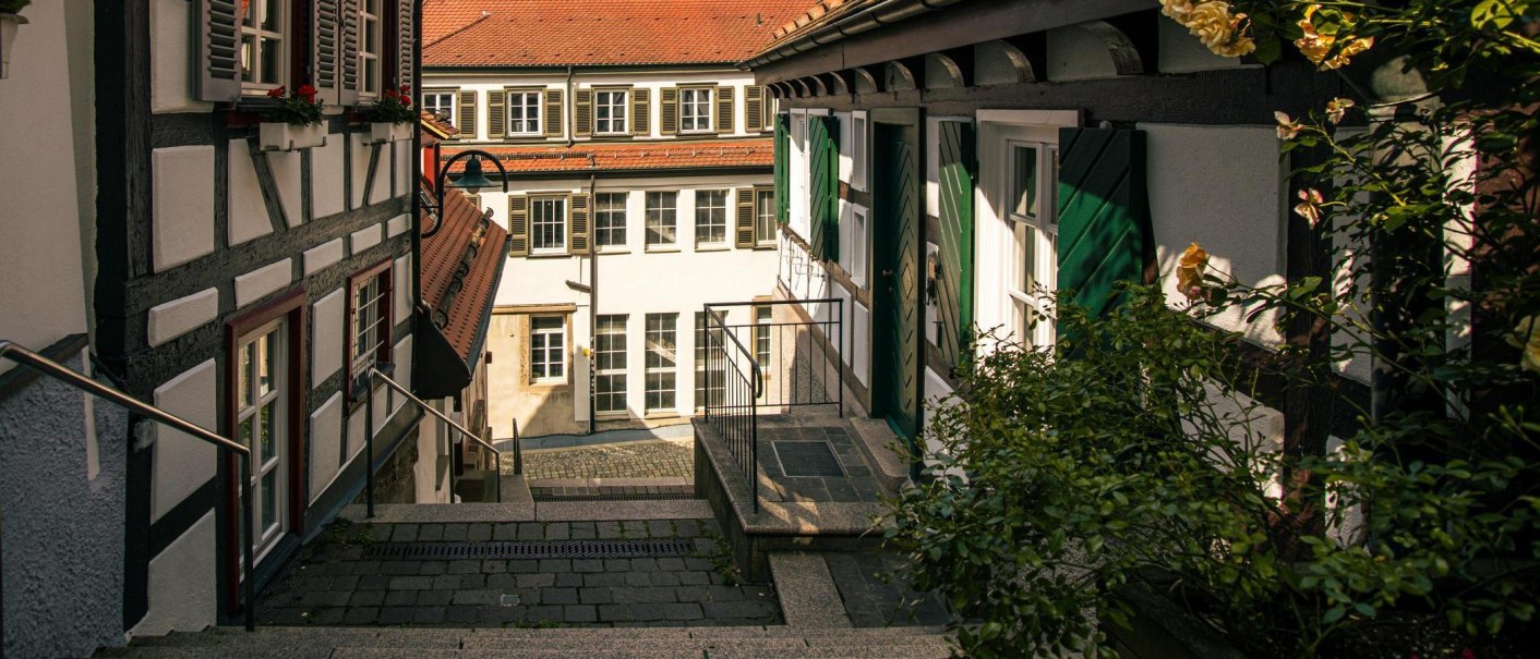 Narrow alley in Herrenberg's old town with half-timbered houses and flowering plants. The shutters are green and the buildings have red tiled roofs., © Stuttgart-Marketing GmbH, Sarah Schmid