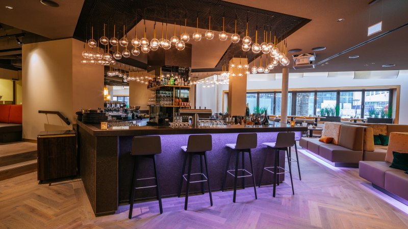 Modern bar with stylish lighting, high stools and cozy seating areas. The atmosphere is inviting and elegant., © Breuninger