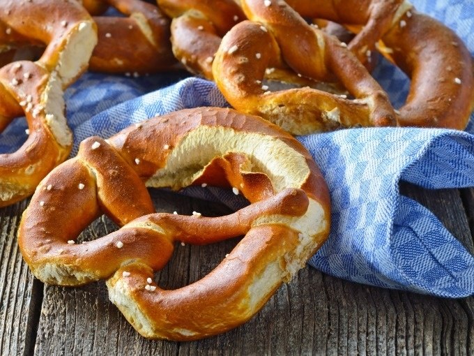 Frische Brezeln liegen auf einem blau-wei&szlig; karierten Tuch auf einem rustikalen Holztisch., &copy; Cool-Tours StattReisen
