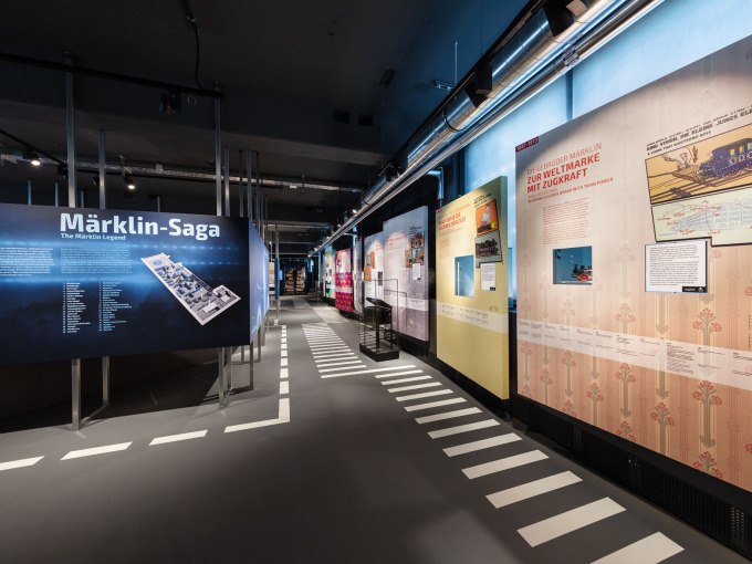 Interior view of the Märklineum with exhibition walls on the history of Märklin and information boards. The room has a modern design and is well lit., © Märklin Spielwaren Vertriebs-GmbH Interior view of the Märklineum with exhibition walls on the history of Märklin and information boards. The room has a modern design and is well lit., © Märklin Spielwaren Vertriebs-GmbH