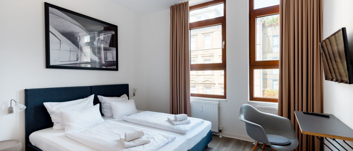 Modernes Doppelzimmer mit zwei Betten, Bild an der Wand, kleinem Tisch und Stuhl. Gro&szlig;e Fenster mit Vorh&auml;ngen., &copy; Hotel Olgaeck