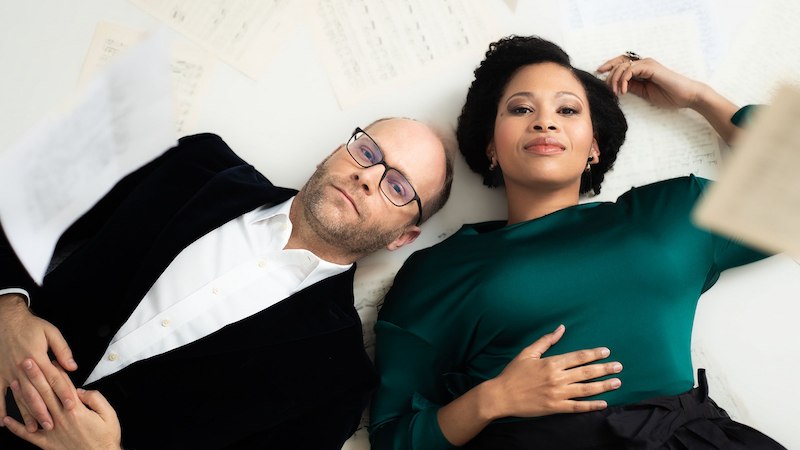 Zwei Personen liegen auf einem wei&szlig;en Hintergrund, umgeben von verstreuten Notenbl&auml;ttern. Sie blicken entspannt in die Kamera., &copy; Internationale Hugo-Wolf-Akademie