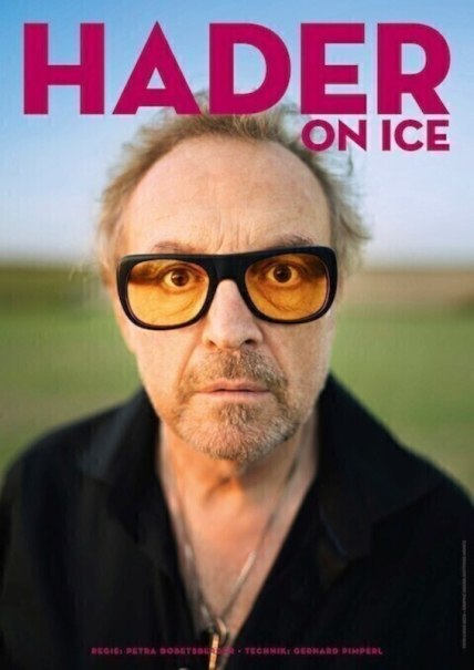 A man with yellow-tinted sunglasses looks seriously into the camera. The background is blurred. At the top is the title 'HADER ON ICE'., © Theaterhaus Stuttgart e.V. A man with yellow-tinted sunglasses looks seriously into the camera. The background is blurred. At the top is the title 'HADER ON ICE'., © Theaterhaus Stuttgart e.V.
