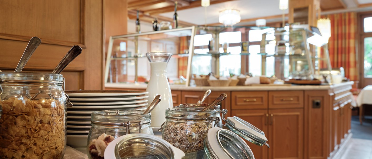 Frühstücksbuffet im Badhotel Restaurant Stauferland mit Gläsern voller Müsli, einer Milchkanne und gestapelten Tellern auf einem Holzfass., © Badhotel Restaurant Stauferland