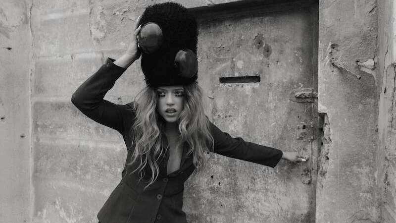 Eine Frau mit einem großen, flauschigen Hut posiert vor einer alten, verwitterten Tür. Sie trägt einen Blazer und hat langes, gewelltes Haar., © Music Circus Concertbüro GmbH & Co. KG Eine Frau mit einem großen, flauschigen Hut posiert vor einer alten, verwitterten Tür. Sie trägt einen Blazer und hat langes, gewelltes Haar., © Music Circus Concertbüro GmbH & Co. KG