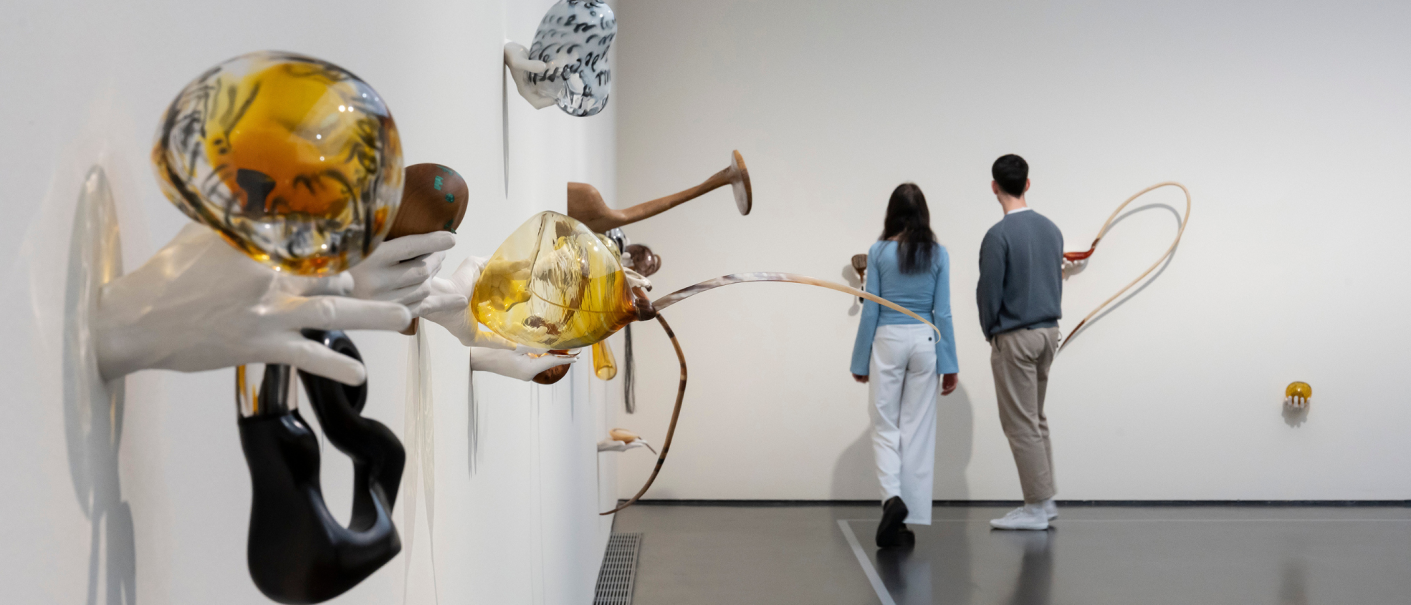 Zwei Personen betrachten eine Wandinstallation mit skulpturalen H&auml;nden und farbigen Glasobjekten in einem modernen Ausstellungsraum., &copy; VG Bild-Kunst, Bonn 2025 /  Foto: Frank Kleinbach, Stuttgart