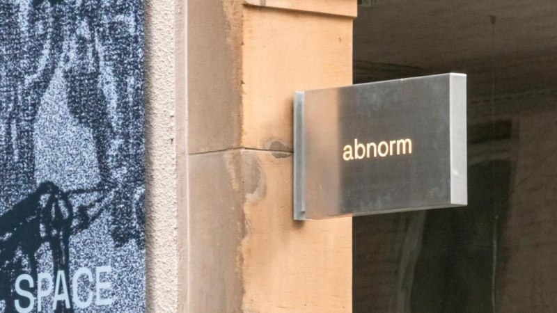 Ein Metallschild mit der Aufschrift 'abnorm' h&auml;ngt an einer Wand. Daneben ist ein Kunstplakat zu sehen., &copy; SMG, Sarah Schmid