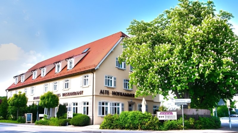 Ein Hotel mit rotem Dach und mehreren Fenstern, umgeben von B&auml;umen und B&uuml;schen, unter blauem Himmel., &copy; Hotel Neuwirtshaus