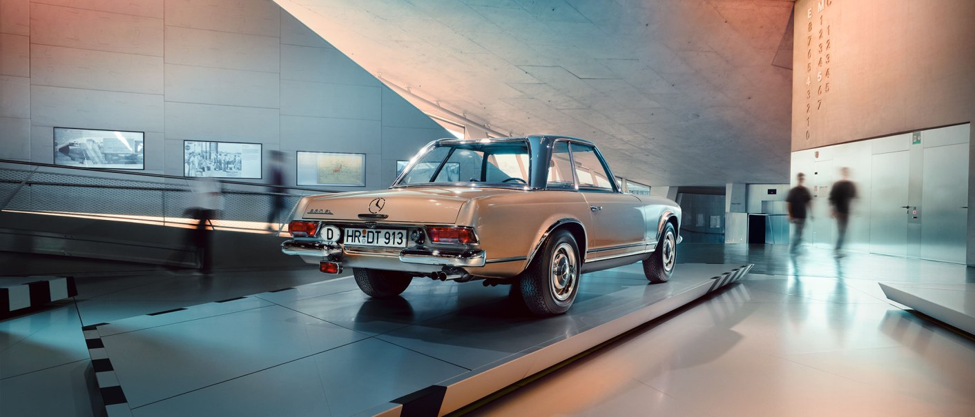 Ein Mercedes-Benz 280 SL steht im modernen Museum ausgestellt. Menschen gehen im Hintergrund vorbei. Die Architektur ist futuristisch., © Mercedes-Benz Heritage GmbH Ein Mercedes-Benz 280 SL steht im modernen Museum ausgestellt. Menschen gehen im Hintergrund vorbei. Die Architektur ist futuristisch., © Mercedes-Benz Heritage GmbH