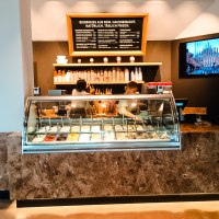 Eisdiele mit Theke, gefüllt mit verschiedenen Eissorten. Zwei Personen arbeiten dahinter. An der Wand ein Menü und ein Bildschirm., © Old Bridge Gelateria Stuttgart Eisdiele mit Theke, gefüllt mit verschiedenen Eissorten. Zwei Personen arbeiten dahinter. An der Wand ein Menü und ein Bildschirm., © Old Bridge Gelateria Stuttgart