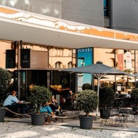 Außenbereich eines Cafés mit Tischen, Stühlen und Sonnenschirmen. Menschen sitzen und entspannen. Pflanzen in Töpfen dekorieren den Bereich., © Stuttgart Marketing GmbH, Sarah Schmid Außenbereich eines Cafés mit Tischen, Stühlen und Sonnenschirmen. Menschen sitzen und entspannen. Pflanzen in Töpfen dekorieren den Bereich., © Stuttgart Marketing GmbH, Sarah Schmid