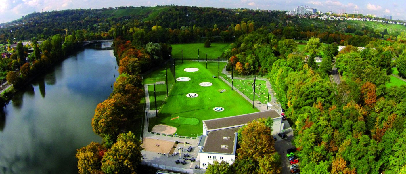 Luftaufnahme eines Golfplatzes in Stuttgart, umgeben von Bäumen und einem Fluss. Im Hintergrund sind Hügel und Gebäude zu sehen., © Citygolf Stuttgart