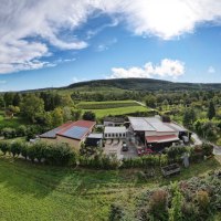 Aerial view of the Eißele vineyard with buildings, fields and trees. Hills and blue sky with clouds in the background., © Weingut Eißele Aerial view of the Eißele vineyard with buildings, fields and trees. Hills and blue sky with clouds in the background., © Weingut Eißele