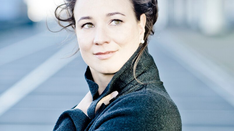 Eine Frau in einem dunklen Mantel blickt nachdenklich in die Ferne. Der Hintergrund ist unscharf und zeigt eine Straße., © Staatliche Hochschule für Musik und Darstellende Kunst Eine Frau in einem dunklen Mantel blickt nachdenklich in die Ferne. Der Hintergrund ist unscharf und zeigt eine Straße., © Staatliche Hochschule für Musik und Darstellende Kunst