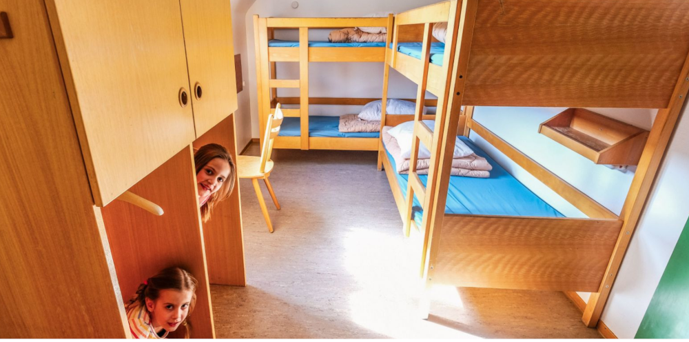 Zwei Etagenbetten in einem hellen Raum, zwei Personen schauen l&auml;chelnd aus einem Schrank hervor., &copy; DJH Baden-W&uuml;rttemberg e.V.