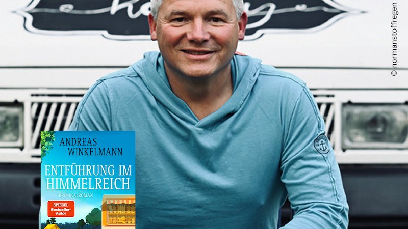 Ein Mann in blauem Hoodie sitzt vor einem Fahrzeug und hält das Buch 'Entführung im Himmelreich' von Andreas Winkelmann. Thalia-Logo sichtbar., © Thalia Deutschland GmbH & Co. KG