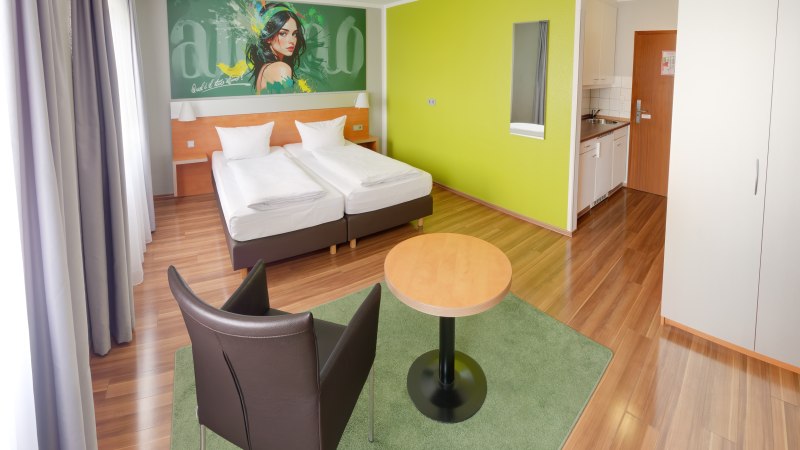Modernes Superior Doppelzimmer mit zwei Betten, grünem Wandbild, Tisch, Stuhl und kleiner Küchenzeile auf Holzboden., © attimo Hotel Stuttgart Modernes Superior Doppelzimmer mit zwei Betten, grünem Wandbild, Tisch, Stuhl und kleiner Küchenzeile auf Holzboden., © attimo Hotel Stuttgart