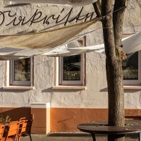 A caf&eacute; with awnings and orange chairs in the outdoor area. The fa&ccedil;ade is beige with lettering. There is a tree in front of the entrance., &copy; Stuttgart-Marketing GmbH, Sarah Schmid