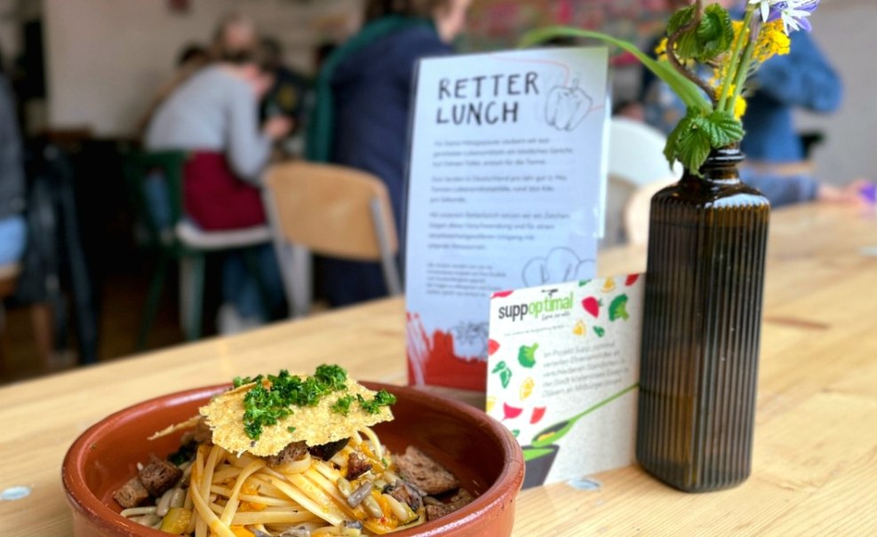 Ein Teller mit Pasta und Kräutern steht auf einem Tisch in einem Café. Daneben eine Vase mit Blumen und ein Schild mit der Aufschrift 'Retter Lunch'., © Foto©Labyrinth
