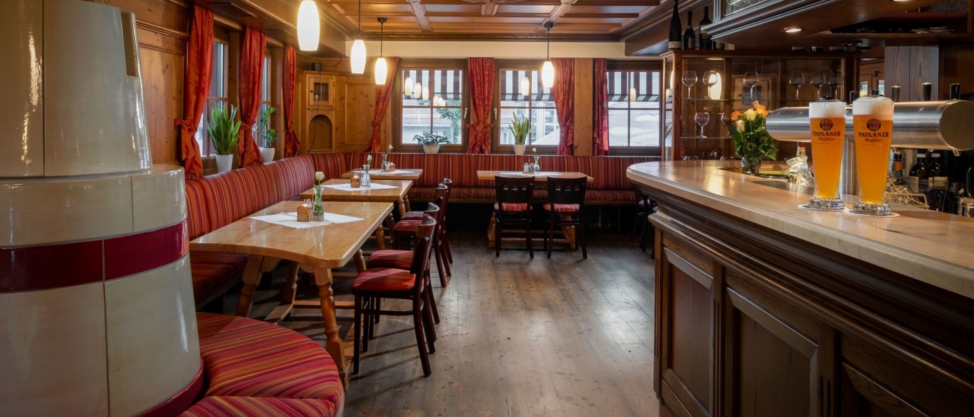 Gem&uuml;tlicher Gastraum mit Holzm&ouml;beln, roten Vorh&auml;ngen und einer Bar. Zwei Biergl&auml;ser stehen auf der Theke. Pflanzen dekorieren den Raum., &copy; Hetzel Hotel Stuttgart
