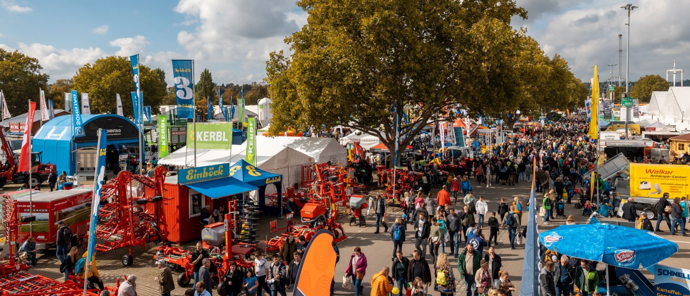 Eine belebte Messe mit zahlreichen Besuchern, St&auml;nden und landwirtschaftlichen Maschinen. Bunte Fahnen und Zelte pr&auml;gen das Bild., &copy; Daniel Schneider, 2022