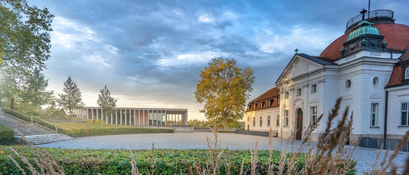 A historic building with a red roof and a modern addition in the background, surrounded by autumn-colored trees and a paved plaza., &copy; &copy; Stuttgart-Marketing GmbH, Martina Denker