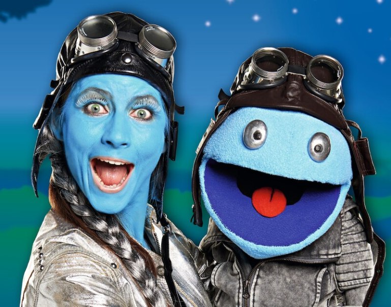 Zwei Figuren mit blauer Haut und Fliegerbrillen l&auml;cheln vor einem Sternenhimmel. Eine ist eine Puppe, die andere eine Person., &copy; Theaterhaus Stuttgart e.V.