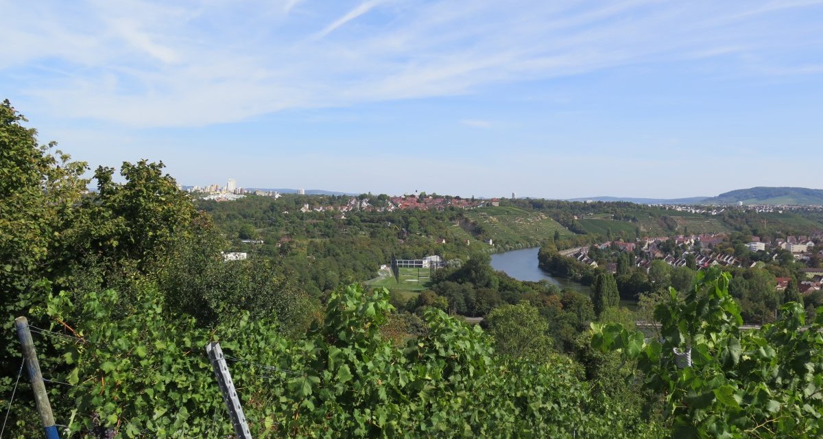 Panoramic view of the Neckar, surrounded by green vineyards and houses under a blue sky., © Stuttgart-Marketing GmbH Panoramic view of the Neckar, surrounded by green vineyards and houses under a blue sky., © Stuttgart-Marketing GmbH