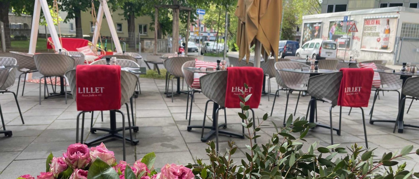 Outdoor seating area with modern chairs and tables, red Lillet blankets and flowers in the foreground. Trees and buildings can be seen in the background., © SMG