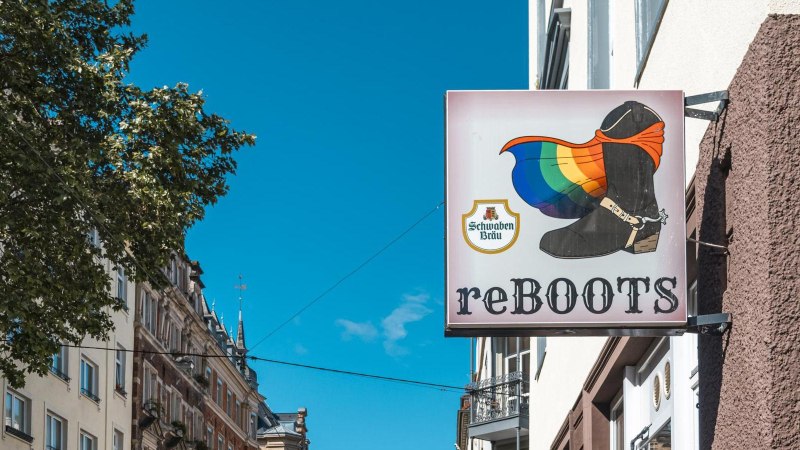 A sign with a boot and a rainbow flag, next to it the inscription 'reBOOTS'. Buildings and a tree can be seen in the background., © SMG Stuttgart Marketing GmbH - Sarah Schmid