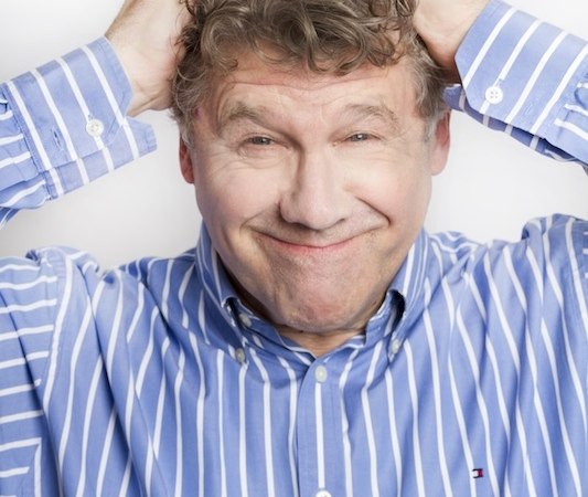 A man in a blue and white striped shirt smiles and holds his head with both hands., © Renitenztheater Stuttgart e.V. A man in a blue and white striped shirt smiles and holds his head with both hands., © Renitenztheater Stuttgart e.V.