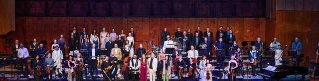 Ein Orchester mit Chor steht auf einer B&uuml;hne in einem Konzertsaal. Die Musiker tragen festliche Kleidung, der Saal ist mit leeren Stuhlreihen gef&uuml;llt., &copy; Marc Sch&auml;fer