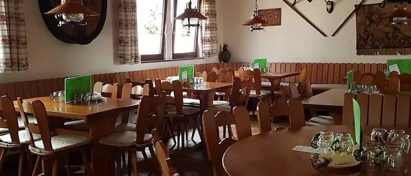 Gemütlicher Gastraum mit Holztischen und Stühlen, rustikale Dekoration, grüne Speisekarten auf den Tischen, Fenster mit Vorhängen., © Weinbau Glock und Sohn GbR