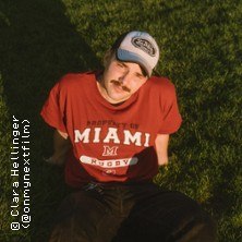 Person mit rotem Miami-Shirt und Baseballkappe sitzt entspannt auf grünem Gras., © links im Bild Person mit rotem Miami-Shirt und Baseballkappe sitzt entspannt auf grünem Gras., © links im Bild
