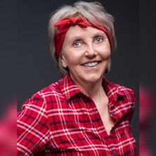 Frau mit grauem Haar, rotem Stirnband und kariertem Hemd l&auml;chelt vor dunklem Hintergrund., &copy; links im Bild
