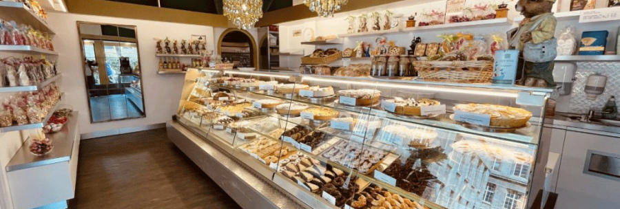 A cozy café with a display case full of pastries and chocolate. Decorative figurines and a chandelier complete the ambience., © FreCla Gastronomiebetriebe GmbH