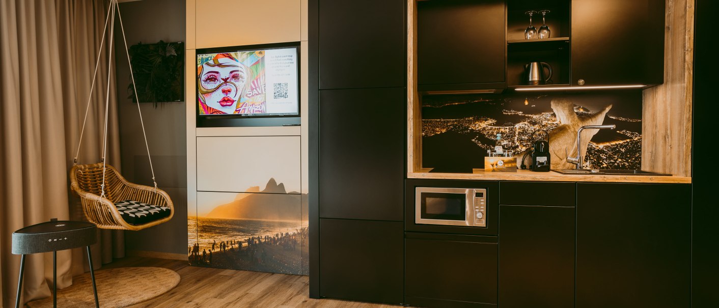 Modern apartment with hanging chair, TV, stylish kitchenette and wooden floor. Decorative murals and cozy atmosphere., © Rioca Stuttgart Posto 4 GmbH Modern apartment with hanging chair, TV, stylish kitchenette and wooden floor. Decorative murals and cozy atmosphere., © Rioca Stuttgart Posto 4 GmbH
