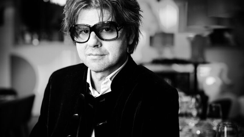 Schwarz-weiß Porträt eines Mannes mit großer Brille und mittellangem Haar in einem eleganten Ambiente., © SWR Big Band Schwarz-weiß Porträt eines Mannes mit großer Brille und mittellangem Haar in einem eleganten Ambiente., © SWR Big Band